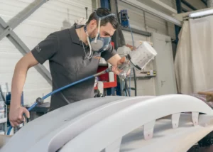 Peintre appliquant la peinture sur un pare-chocs en cabine – Carrosserie Tropea à Chambéry